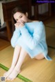 A woman in a blue sweater sitting on the floor.