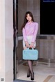 A woman in a pink shirt and white skirt holding a blue briefcase.