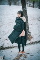 A woman standing in the snow wearing a black coat.