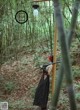 A woman in a black dress holding a sword in a bamboo forest.