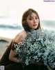 A woman sitting on a beach holding a bunch of flowers.