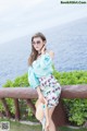 A woman in a blue top and floral skirt posing for a picture.