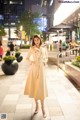 A woman in a beige trench coat is standing on a sidewalk.