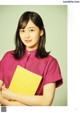 A woman in a pink shirt holding a yellow book.