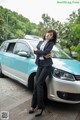 A woman in a business suit leaning against a car.