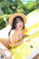 A woman in a yellow bikini and straw hat laying on a yellow boat.