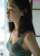 A woman in a gray tank top looking out a window.