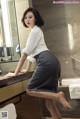 A woman in a white shirt and gray skirt posing in a bathroom.