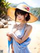 A woman in a blue dress and a straw hat on a beach.