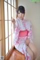 A woman in a pink and white kimono sitting on a window sill.