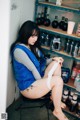 A woman sitting on a chair in front of a shelf of liquor bottles.