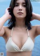 A woman in a white bikini posing by the water.