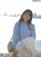 A woman standing next to a body of water holding a bag.