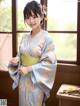 A woman in a blue kimono standing in front of a window.